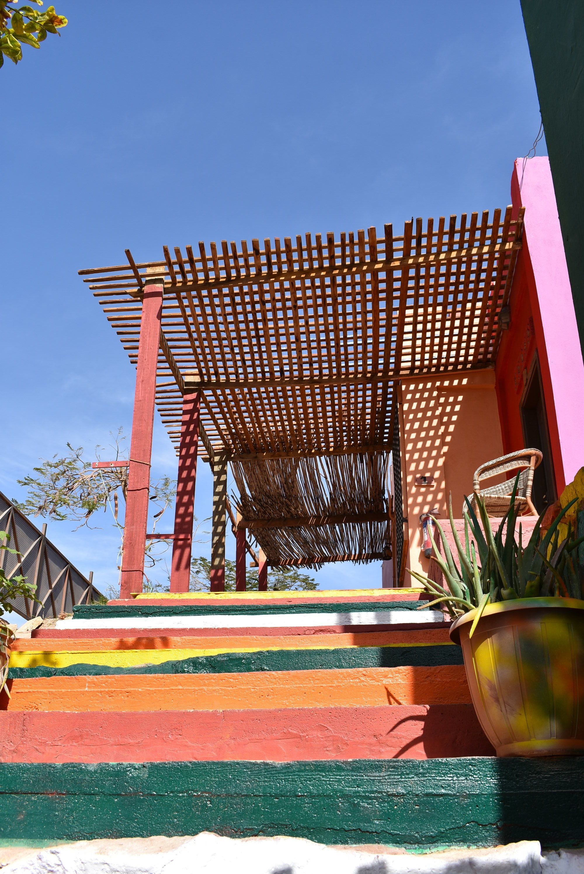 A colorful outdoor area with a wooden pergola, a chair, and a potted plant.