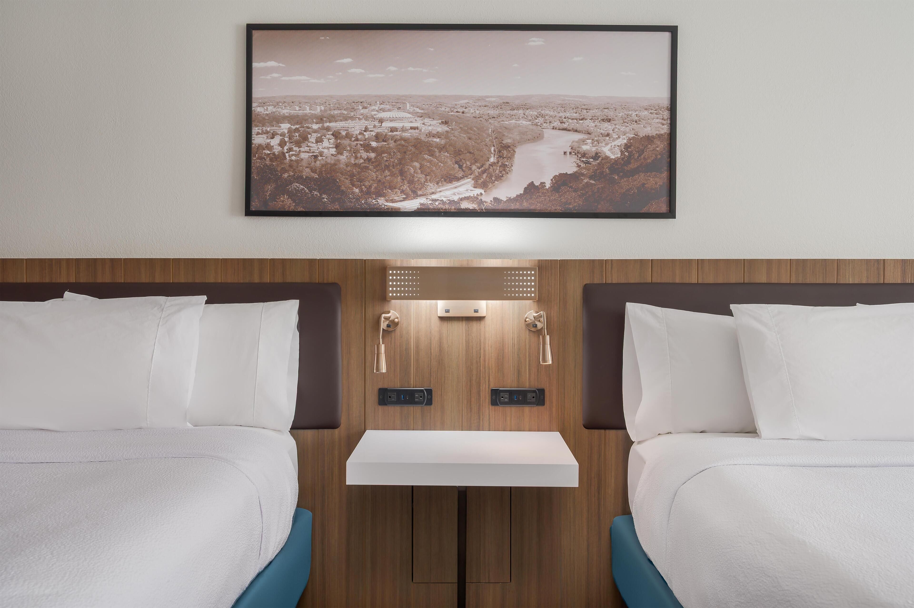 A hotel room with two beds, a small bedside table, a wall-mounted picture, and a wooden panel design.