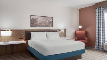 A hotel room with a bed, a nightstand, a chair, a lamp, and a wall-mounted picture.