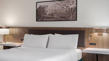 Una habitación de hotel con una cama, una mesita de noche, una lámpara de pared y un cuadro enmarcado sobre la cama.
