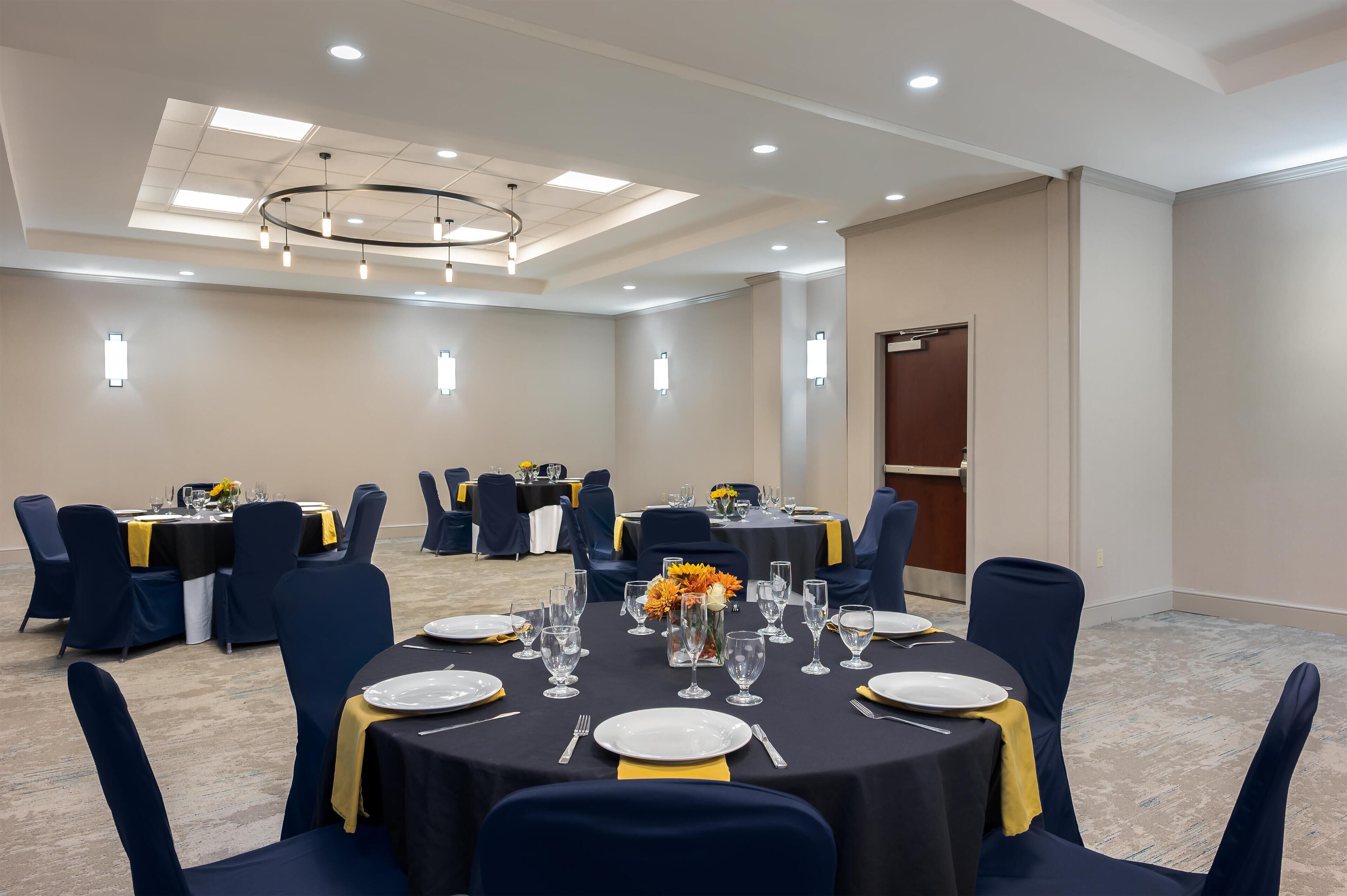 A conference room with round tables, navy blue chairs, and a chandelier.