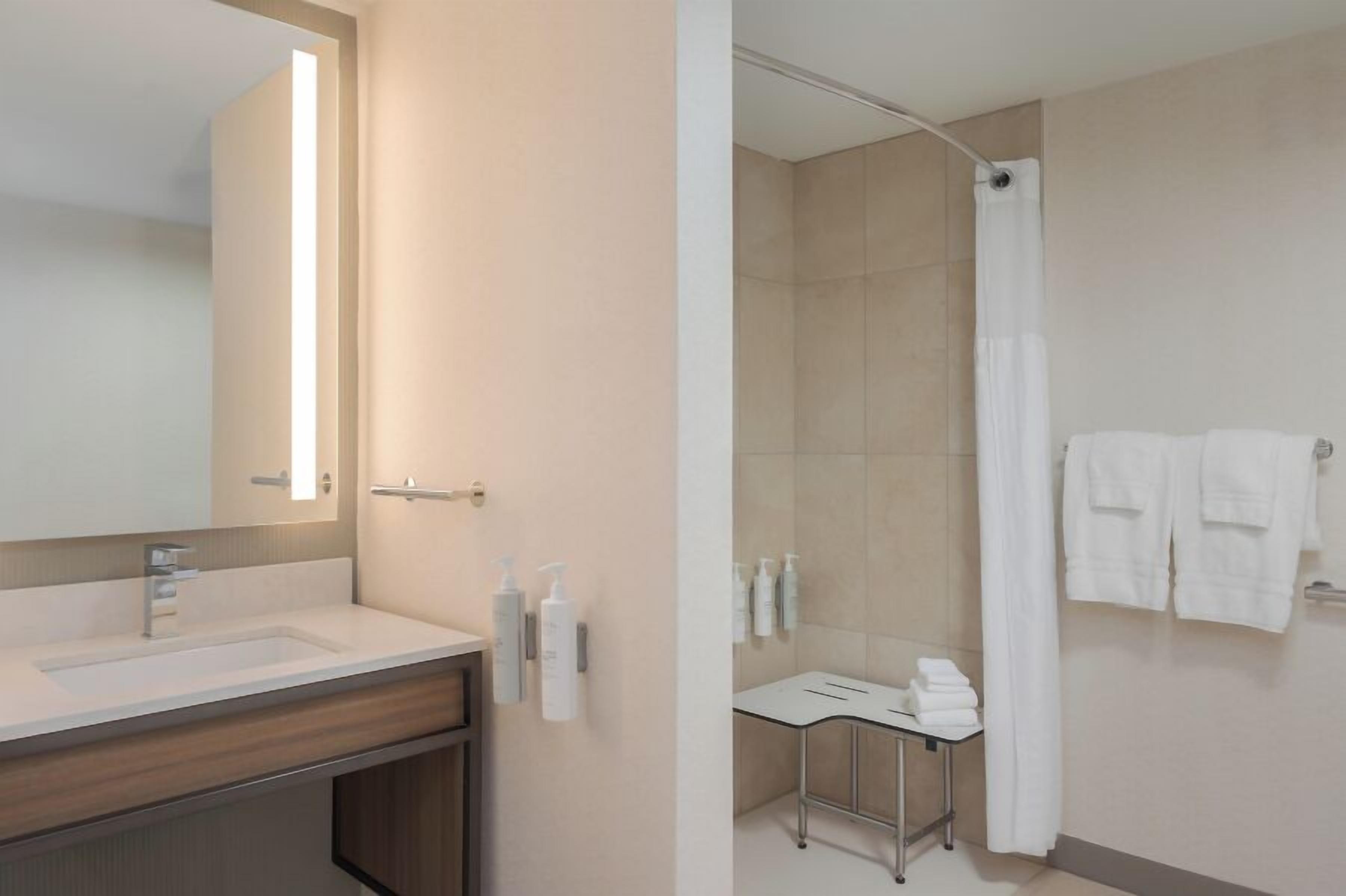 Un baño con lavamanos, espejo, artículos de aseo, ducha y toallero.