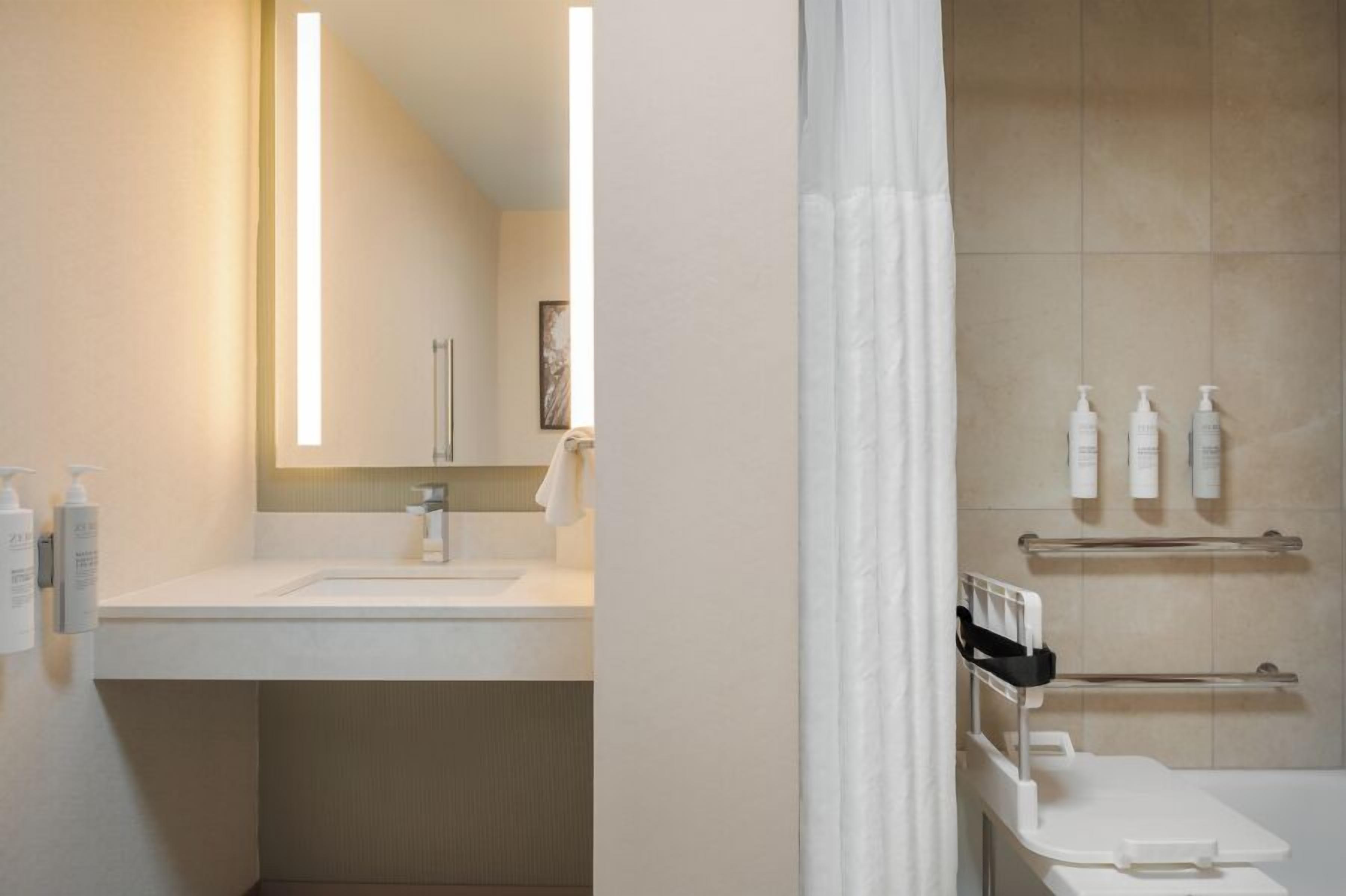 A bathroom with a sink, mirror, shower, and towel rack.