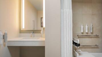 A bathroom with a sink, mirror, shower, and towel rack.