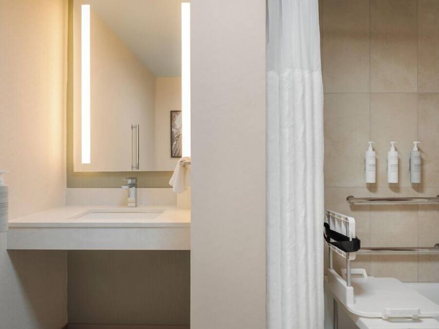 A bathroom with a sink, mirror, shower, and towel rack.