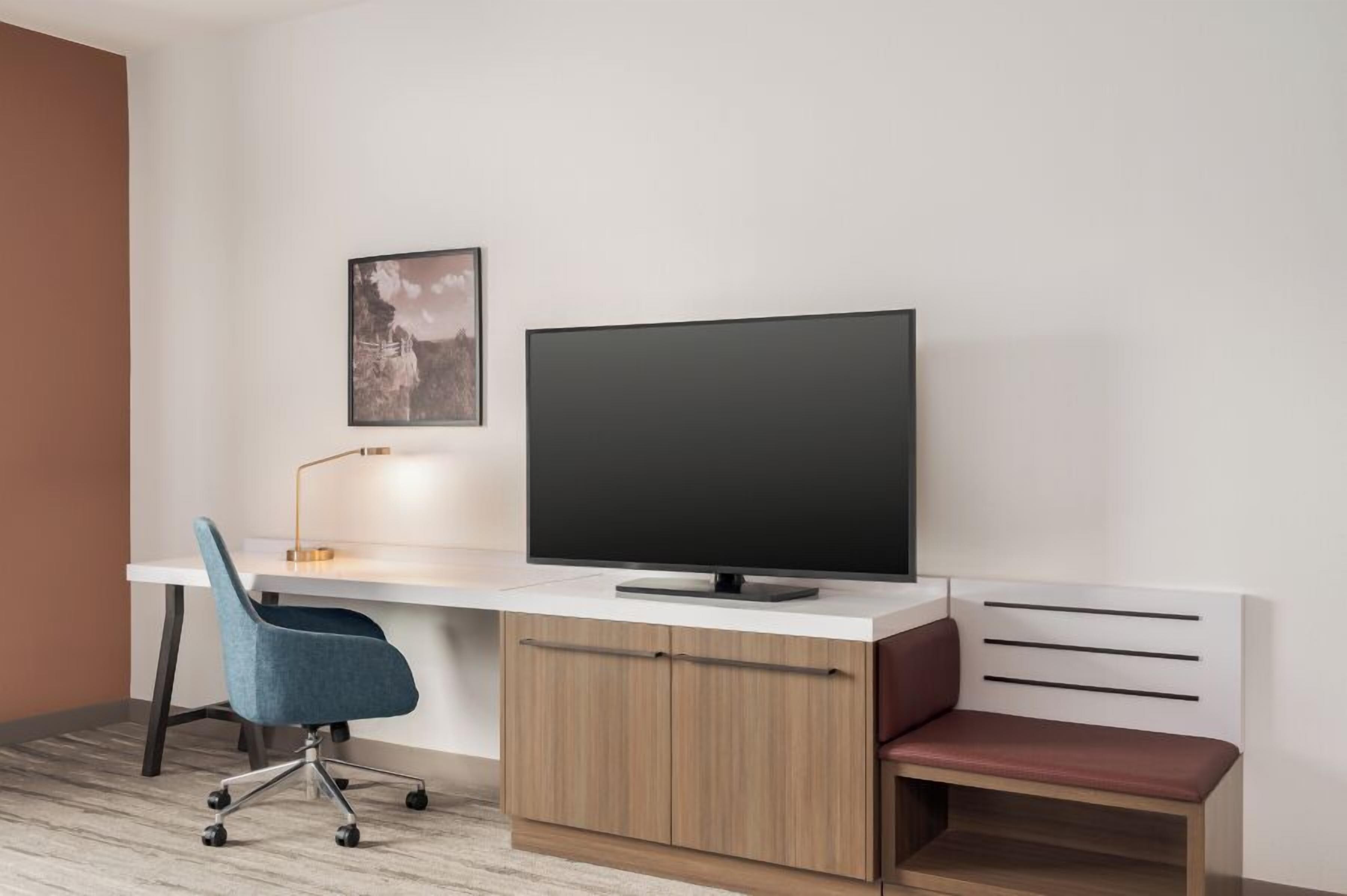 A modern office space with a desk, chair, TV, and a bench.