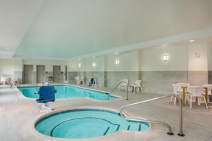 An indoor swimming pool with a blue chair, white lounge chairs, and a table with chairs.