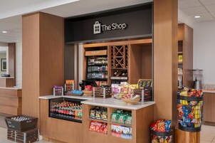 A store named 'The Shop' with a chilled section, shelves of snacks, and a variety of bottled beverages.