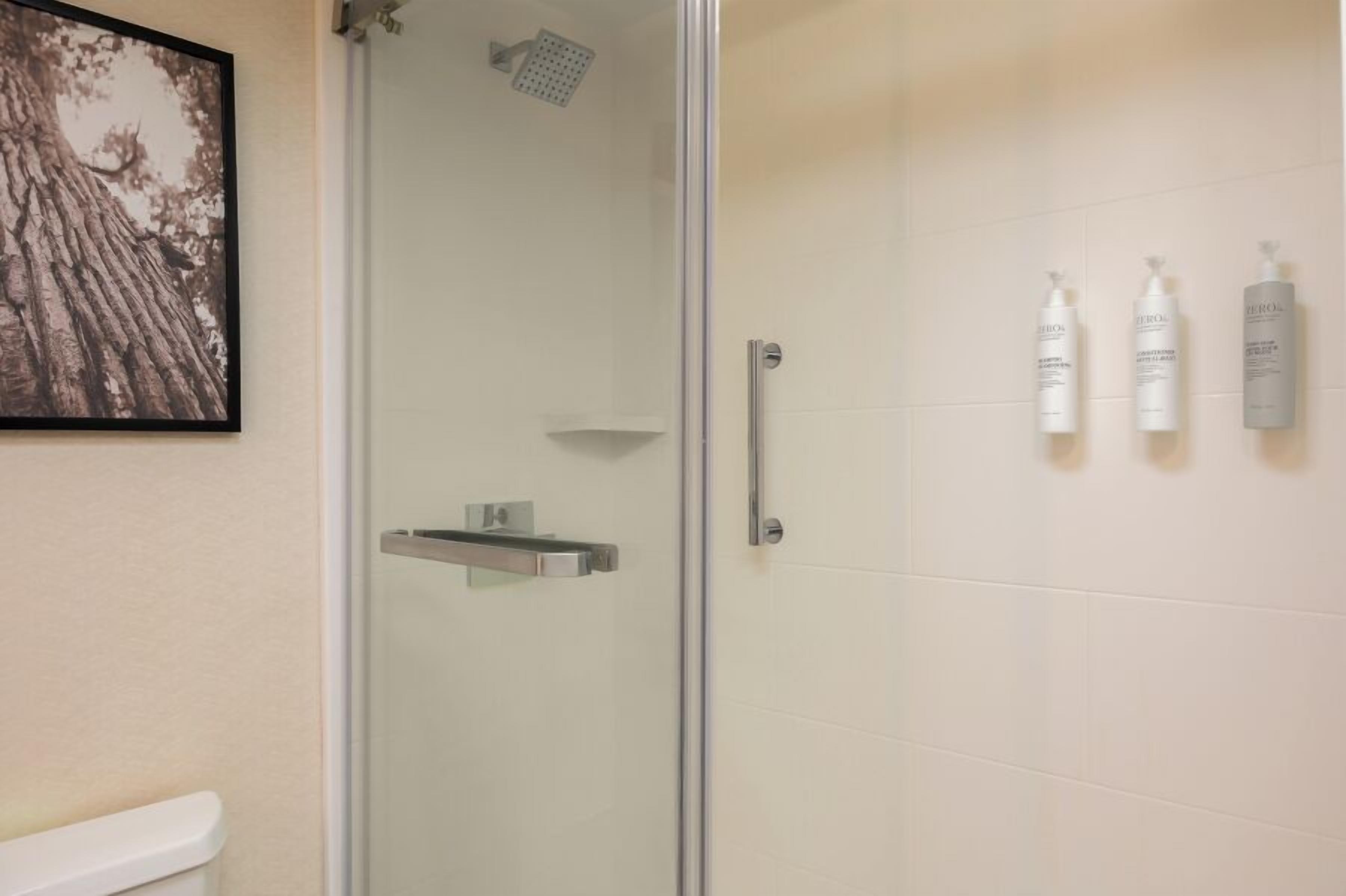 Un baño con cabina de ducha de vidrio, un inodoro y tres botellas de artículos de tocador en la pared.