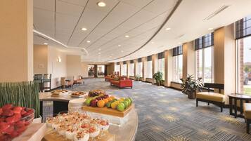 Un hall d’hôtel avec un espace buffet, des sièges et de grandes fenêtres.