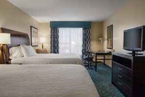 A hotel room with two beds, a desk, a television, and a chair.