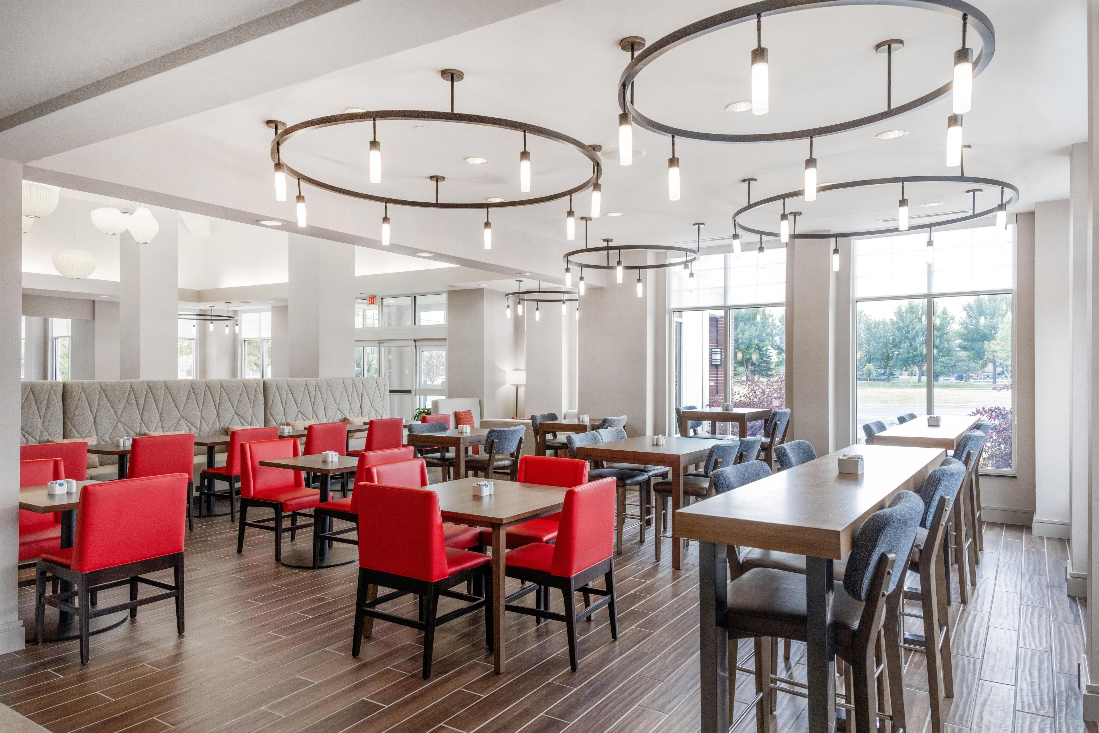 A modern restaurant interior with high ceilings, circular light fixtures, and a mix of red and grey seating.