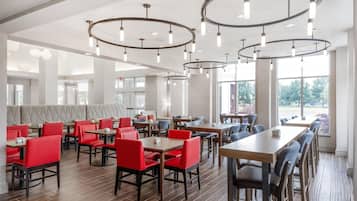 A modern restaurant interior with high ceilings, circular light fixtures, and a mix of red and grey seating.