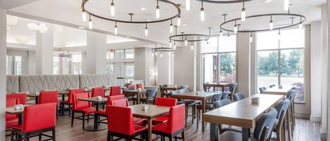 Un interior de restaurante moderno con techos altos, luminarias circulares y una combinación de asientos rojos y grises.