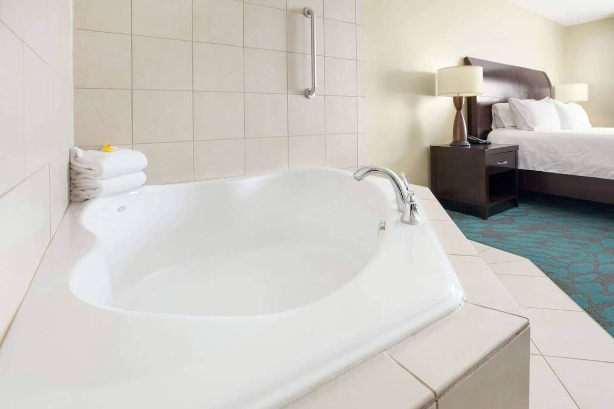 A hotel room with a large bathtub, a bed with a headboard, bedside tables, and a nightstand.