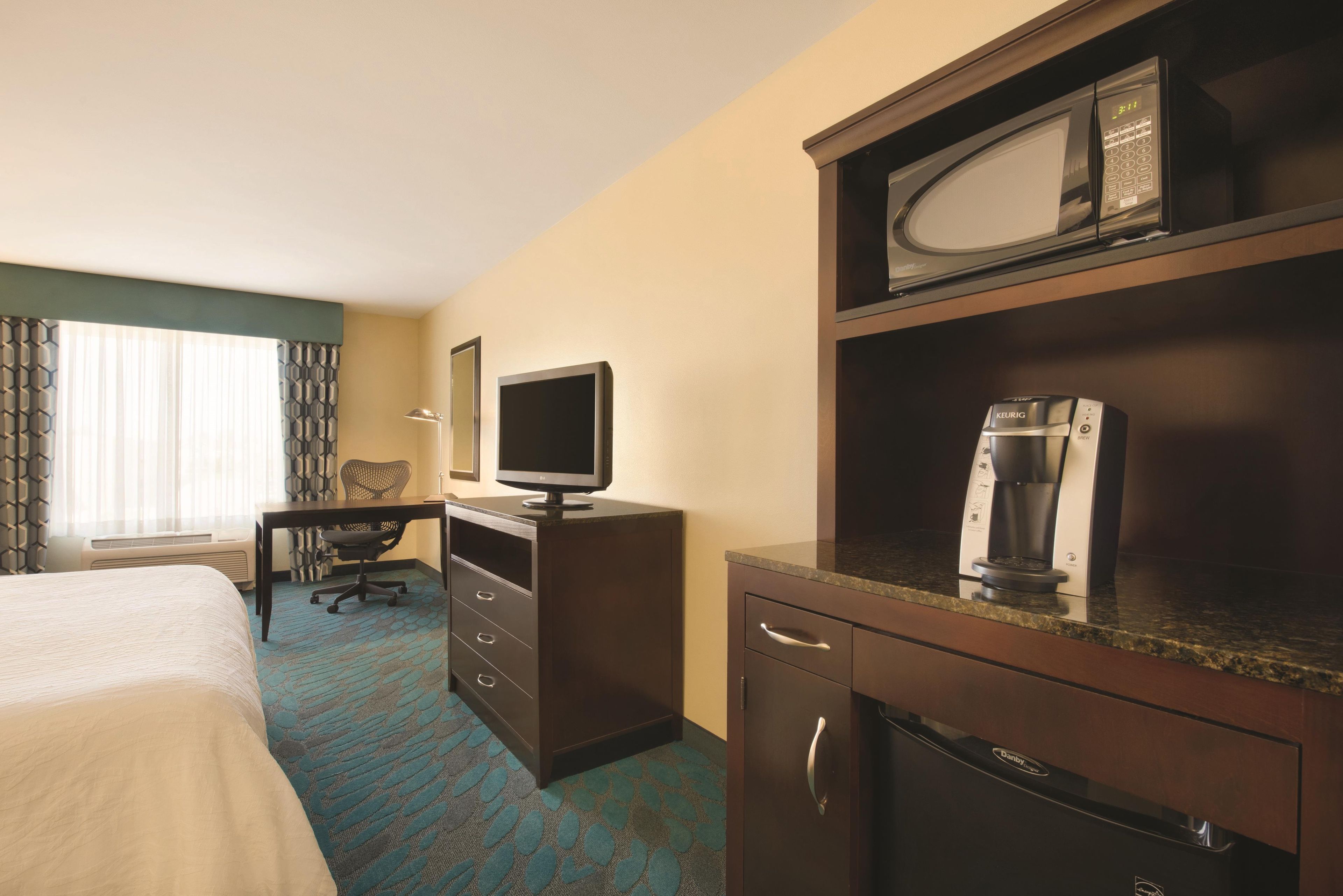 A hotel room with a bed, a desk, a television, a coffee maker, and a microwave.