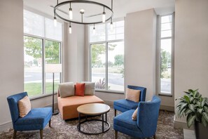 A modern lounge area with a sofa, two armchairs, a coffee table, and large windows offering a view of the outdoors. - Hilton Garden Inn Fargo (Fargo)