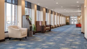 A hotel lobby with a long corridor, seating area with chairs and a sofa, a reception desk, and large windows. - Hilton Garden Inn Fargo (Fargo)
