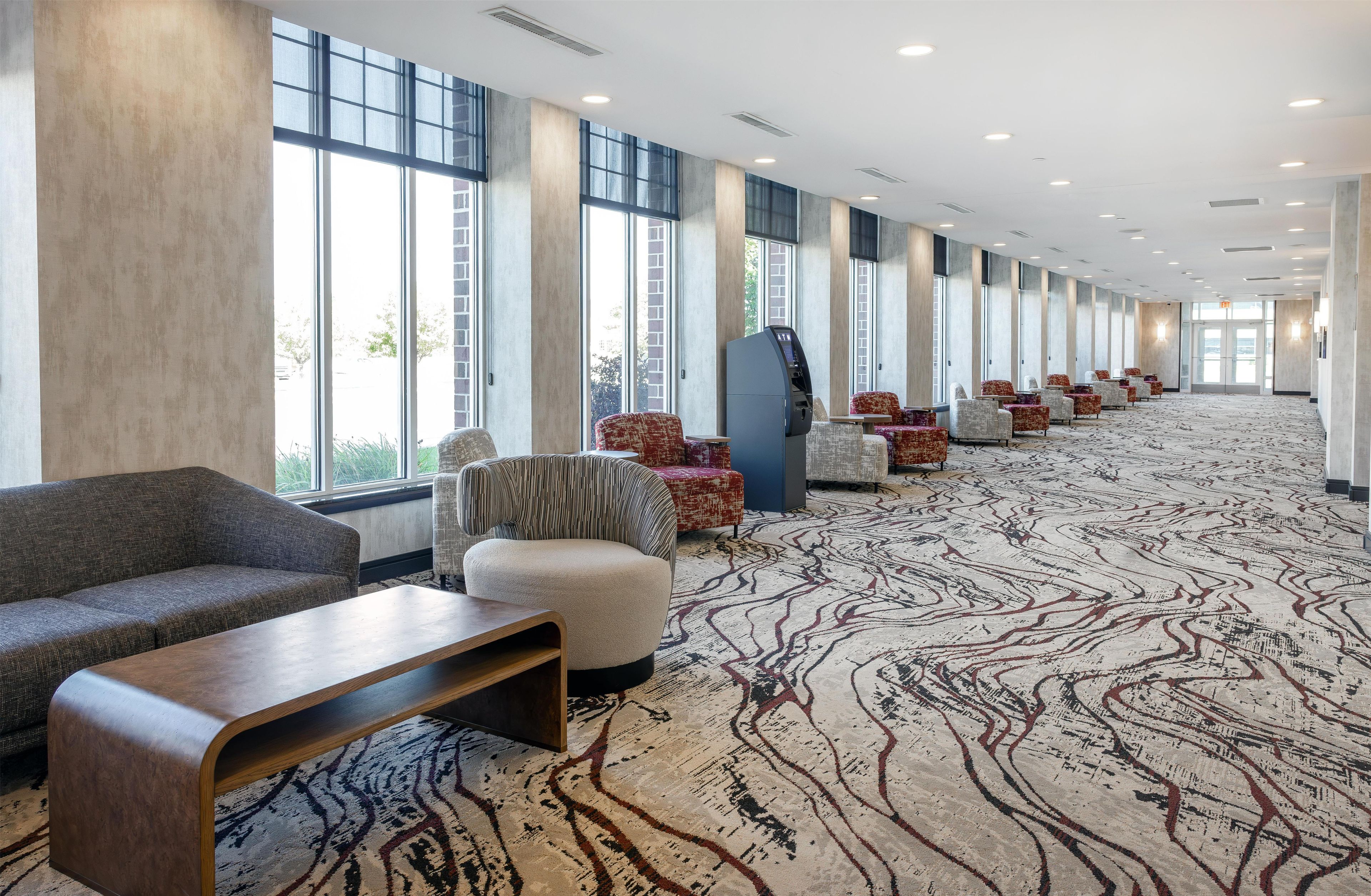 A hotel lobby with a long row of seating, a self-service kiosk, and large windows.