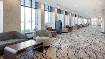 A hotel lobby with a long row of seating, a self-service kiosk, and large windows.