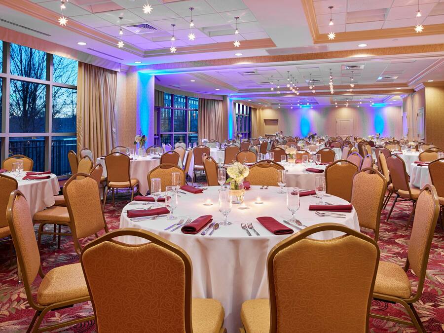 A banquet hall with round tables, chairs, and a carpeted floor.