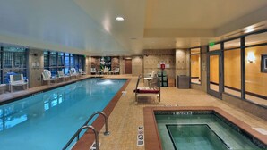 Une piscine intérieure dotée de chaises longues, d’un jacuzzi et d’un espace de réception avec un comptoir et des chaises.