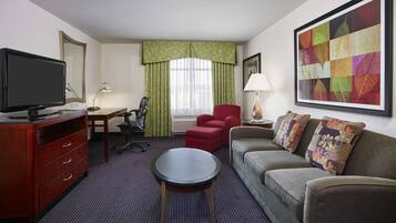 Une chambre d’hôtel équipée d’un bureau, d’une télévision, d’un canapé, d’un fauteuil rouge et d’une grande œuvre d’art encadrée accrochée au mur.