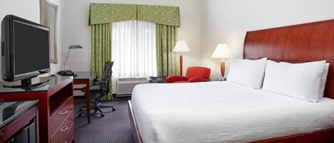A hotel room with a bed, a desk with a television, a chair, two lamps, and a window with curtains.