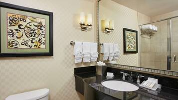 A modern bathroom with a black sink, white toilet, and a large mirror. There are two wall-mounted towel racks with white towels, and a framed artwork above the mirror.