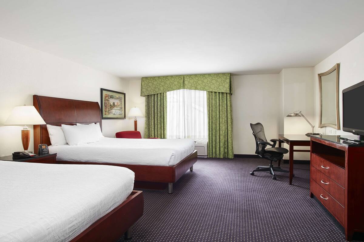 Une chambre d’hôtel avec deux lits, un bureau, une chaise, une commode et un téléviseur.
