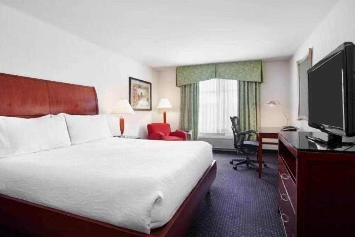 Une chambre d’hôtel avec un grand lit, un bureau avec une chaise, une télévision et une fenêtre avec des rideaux.