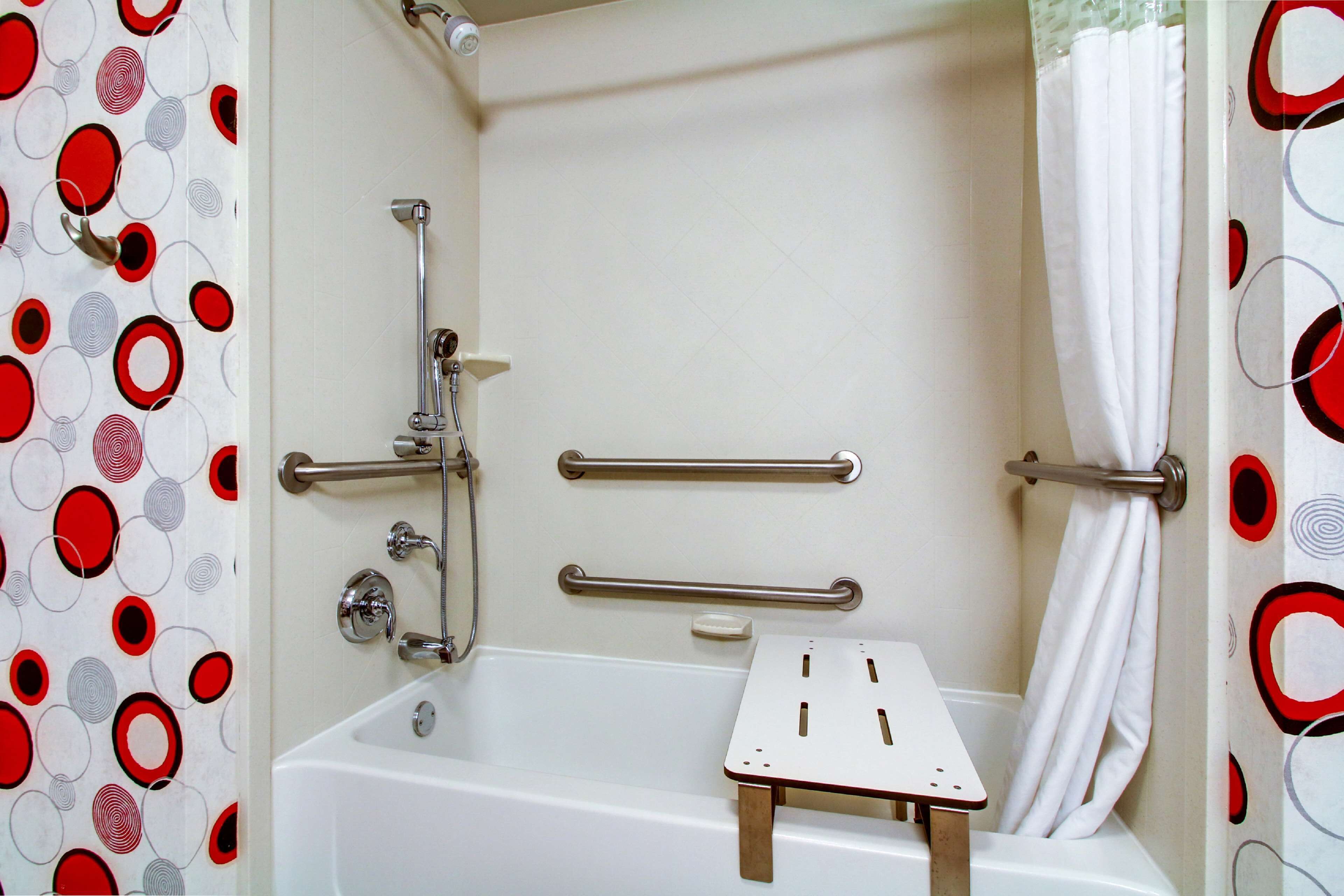 A bathroom with a bathtub, grab bars, and a shower curtain.