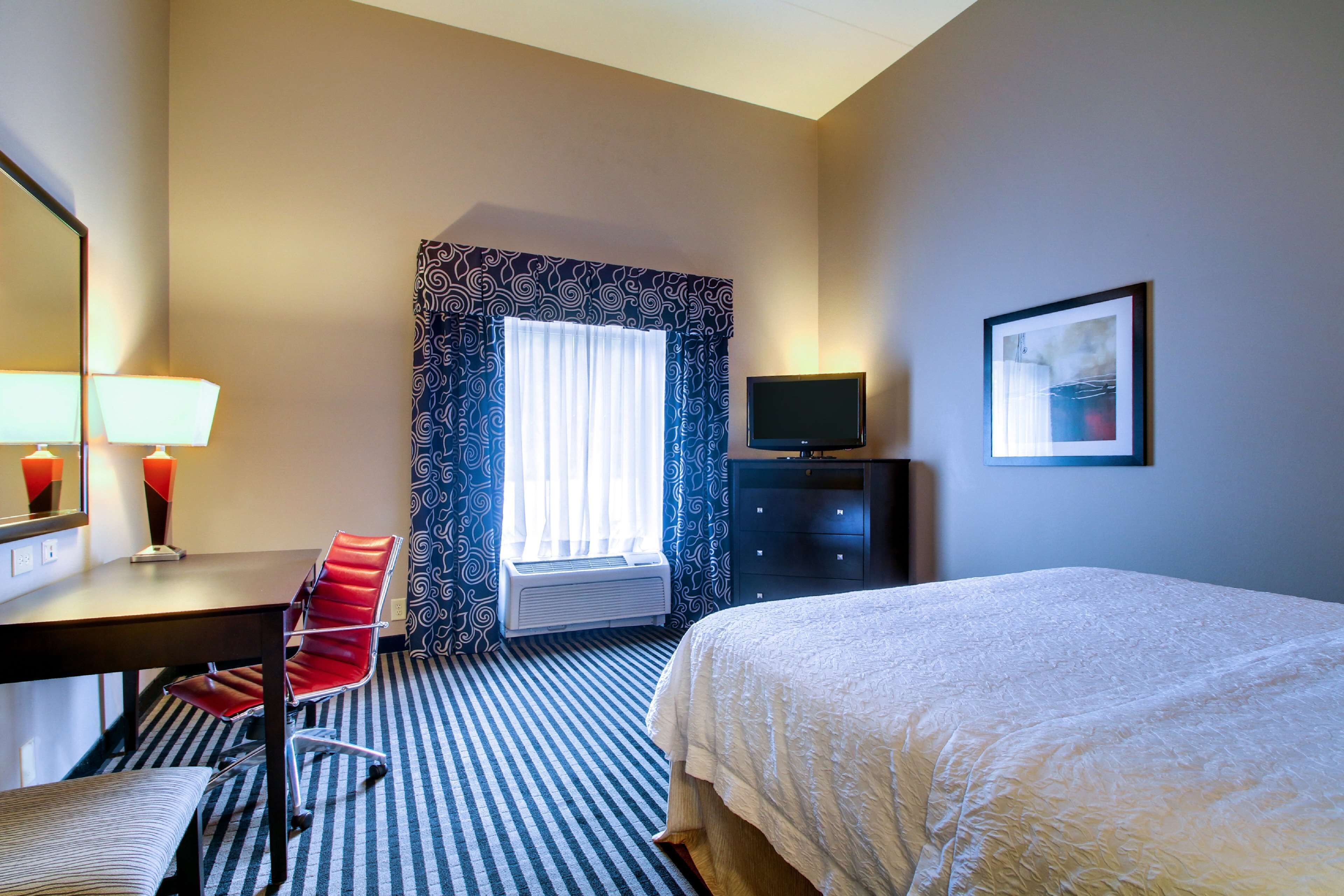 Una camera d'albergo con un letto, una scrivania con una sedia, una televisione e una finestra con tende.