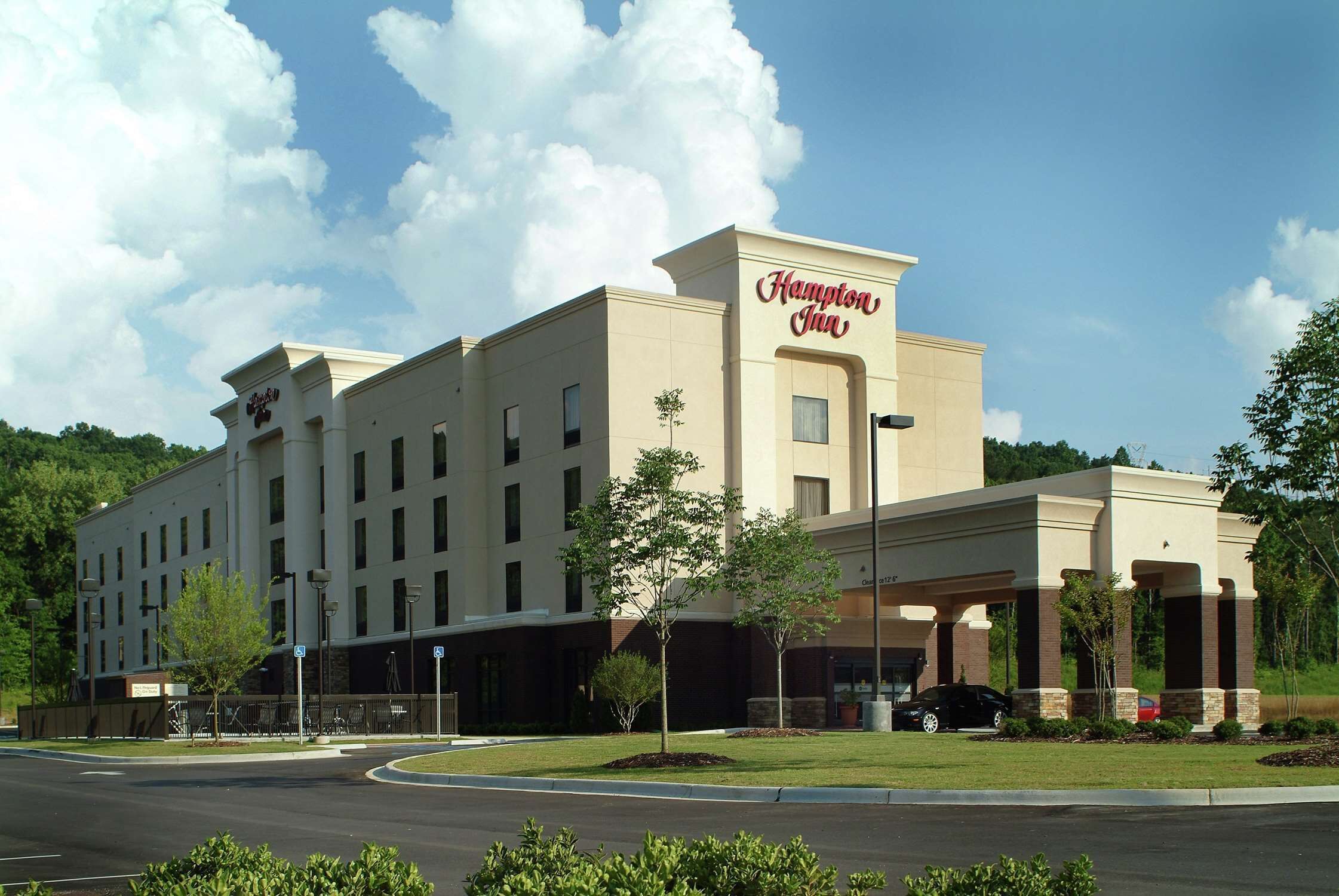 Un hotel Hampton Inn con un diseño moderno, que destaca por su entrada principal y zona de estacionamiento.