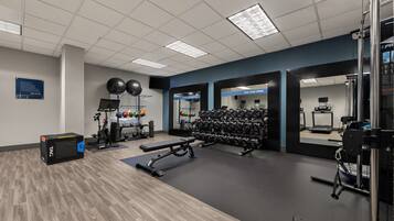 A gym with exercise equipment, a bench, and a wall-mounted mirror.