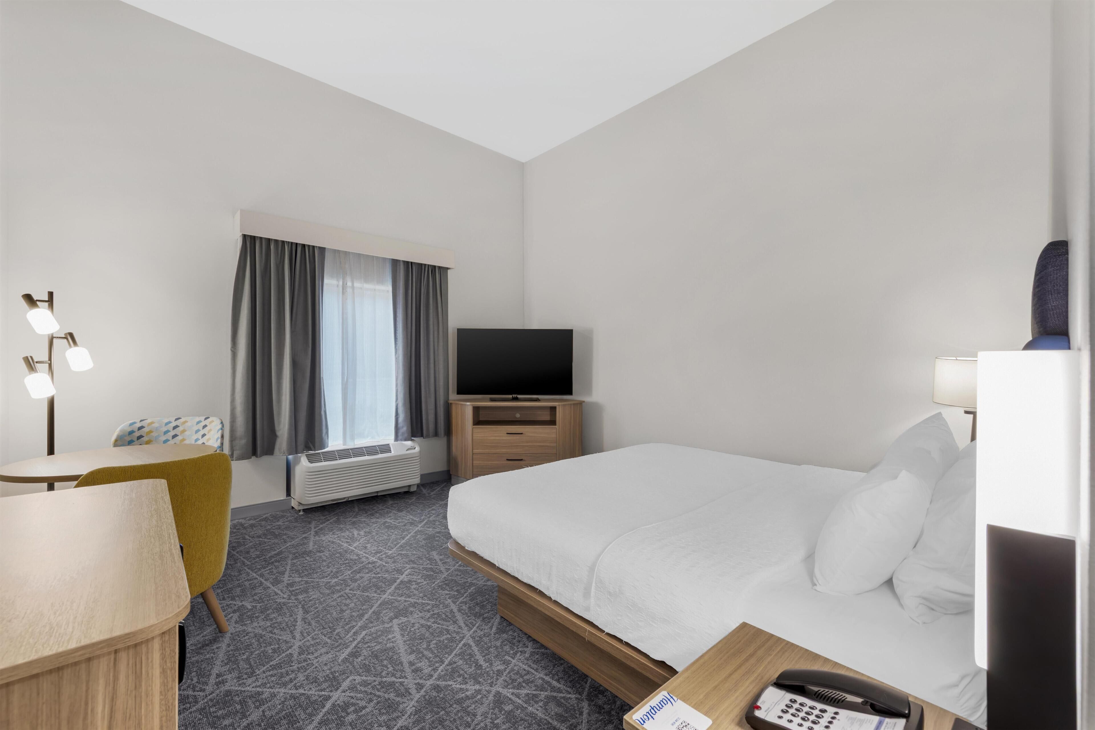 A hotel room with a bed, a desk, a chair, a television, a telephone, and a window with curtains.