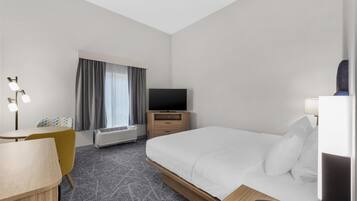 A hotel room with a bed, a desk, a chair, a television, a telephone, and a window with curtains.
