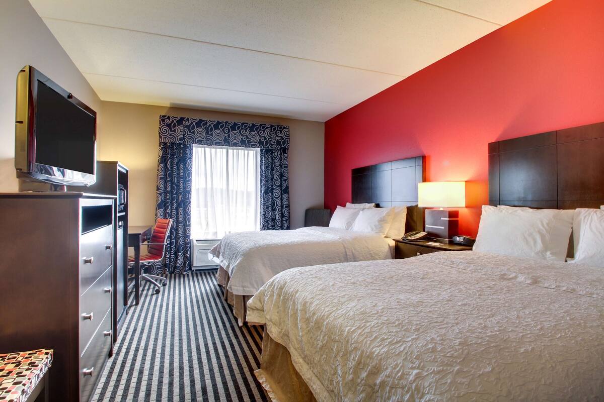 A hotel room with two beds, a desk with a chair, a television, and a window with curtains.