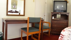 A hotel room with a wooden desk, a chair, a dresser, and a television on top of the dresser. - Budget Inn (Christiansburg)