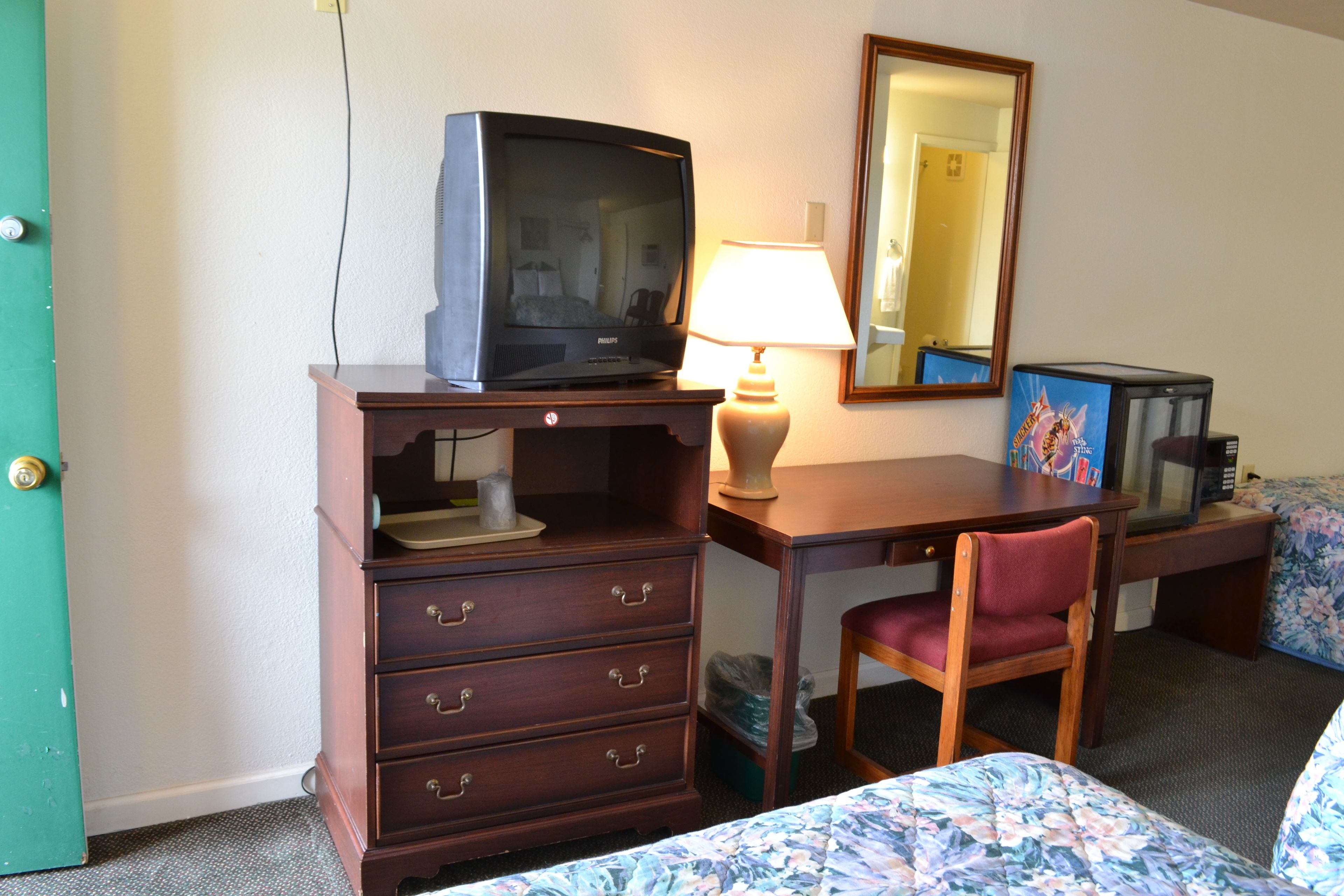 Une chambre d’hôtel avec un bureau en bois, une télévision, une lampe, une chaise et un lit avec une literie à motifs floraux.