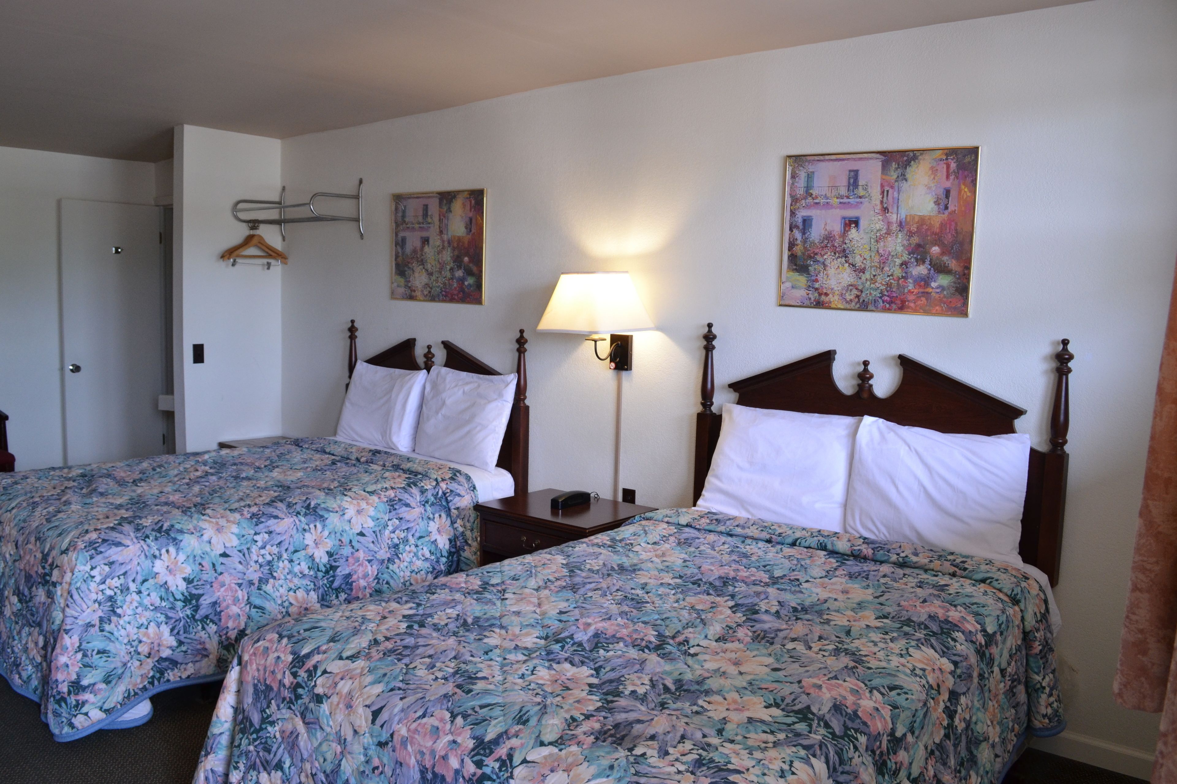 A hotel room with two beds, floral bedspreads, a bedside lamp, and two paintings on the wall.