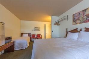 A hotel room with two beds, a desk, a chair, a coat rack, and a painting on the wall.