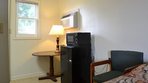 A compact room with a small table, a refrigerator, a microwave, a lamp, and a chair. - Budget Inn (Christiansburg)