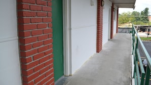 A corridor with a green door, white walls, and red brick accents. - Budget Inn (Christiansburg)