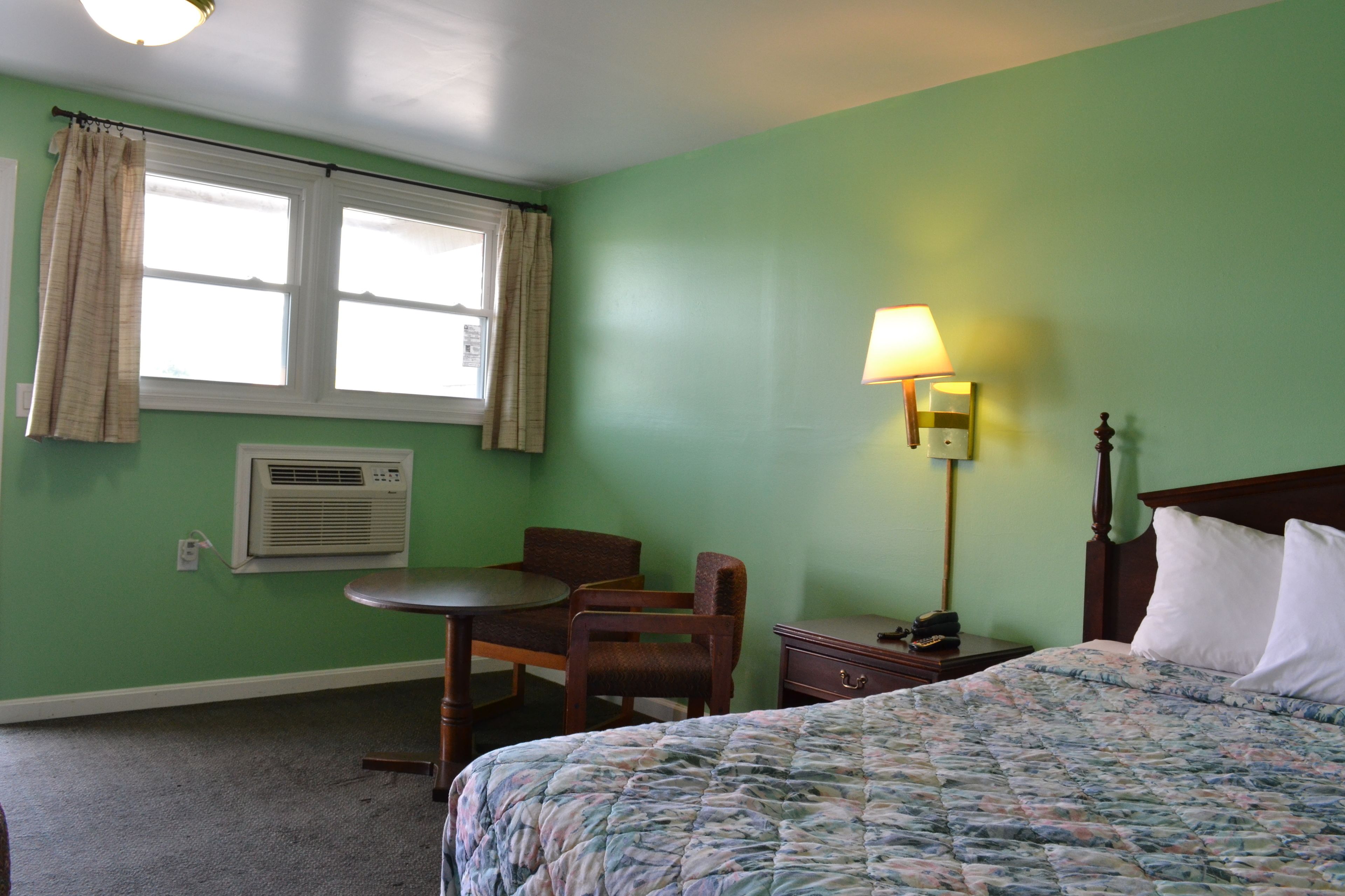A room with a bed, a desk, a chair, a lamp, and a window with curtains.