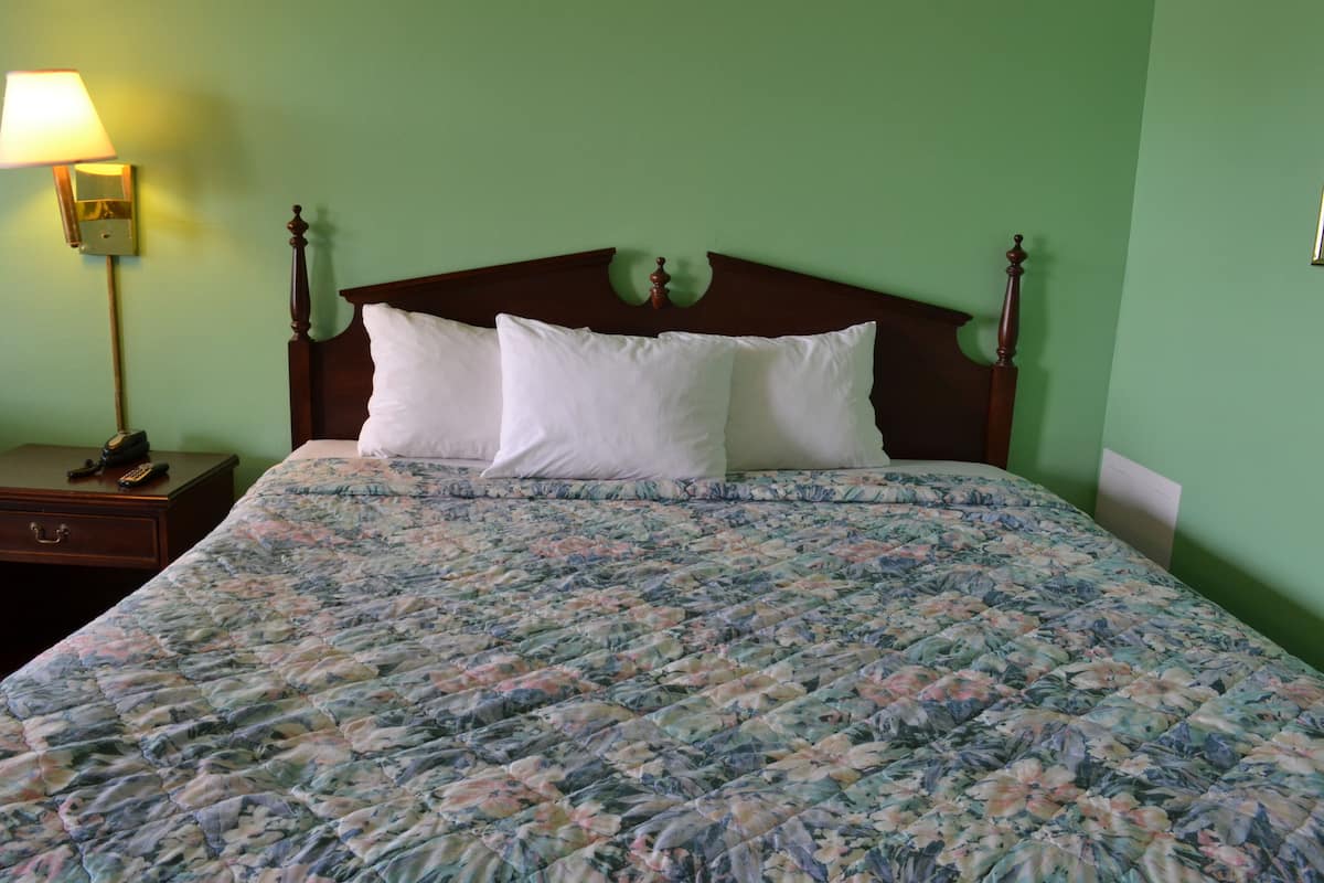 A bed with a floral bedspread, a wooden headboard, and a nightstand with a lamp and a telephone.