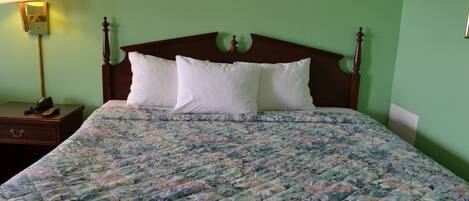 A bed with a floral bedspread, a wooden headboard, and a nightstand with a lamp and a telephone.