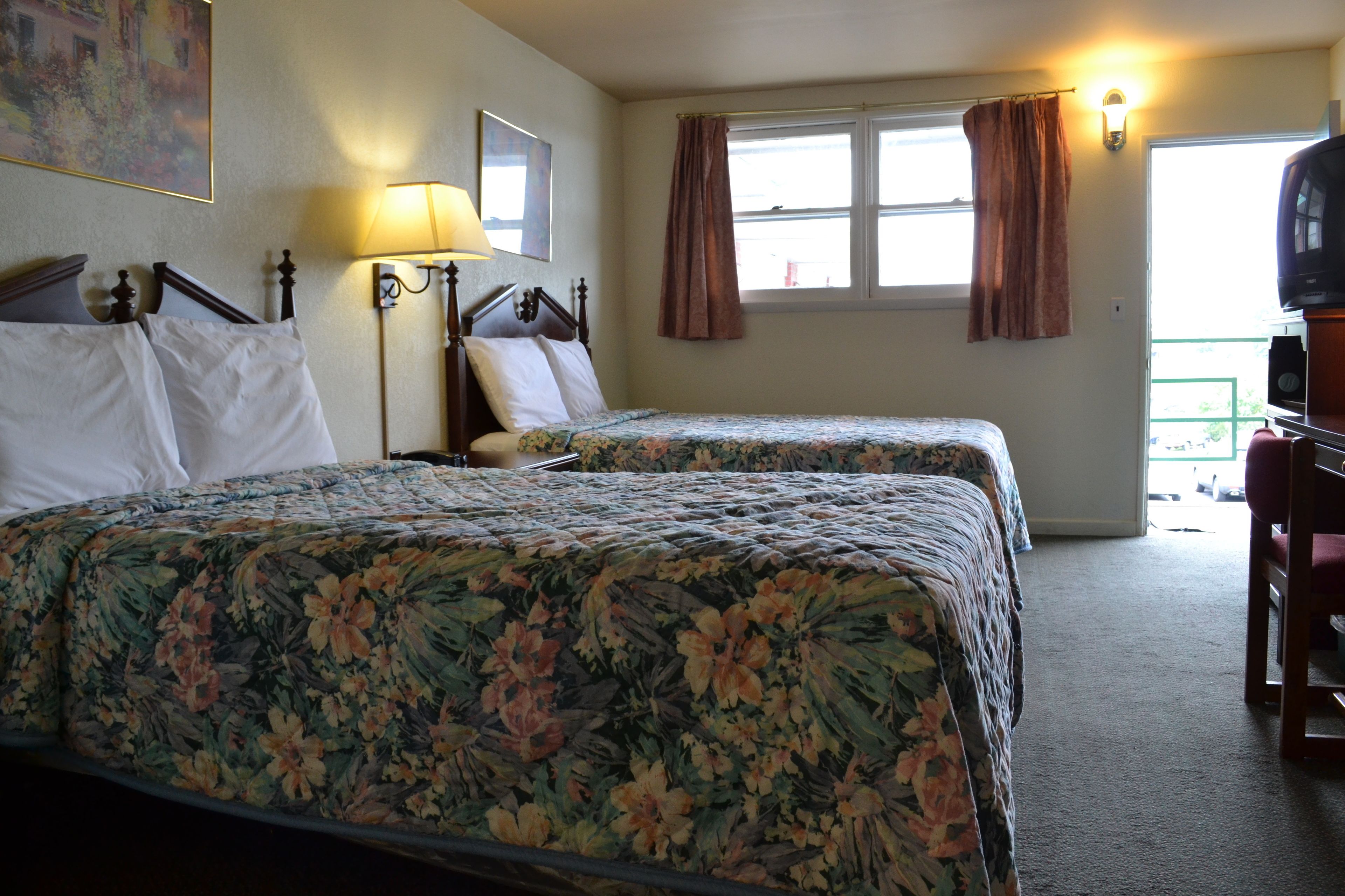 Habitación de hotel con dos camas, un escritorio, una lámpara y un televisor.