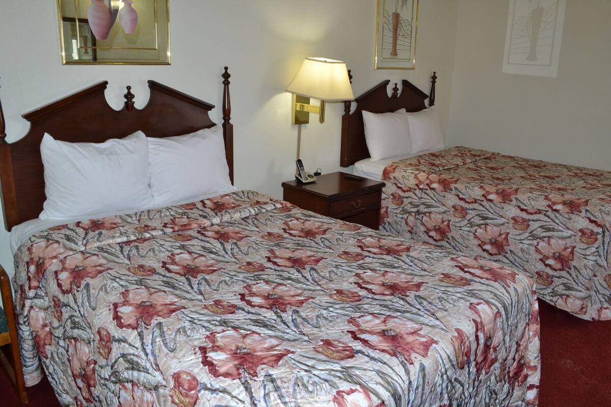 A hotel room with two beds, each with floral bedding, wooden headboards, bedside tables with lamps, and a mirror on the wall.