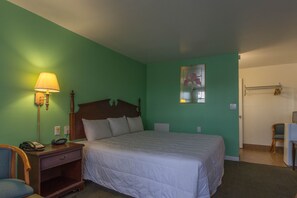 A hotel room with a bed, a nightstand with a lamp, a chair, and a small desk with a chair.